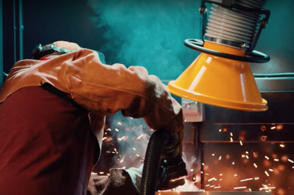 A welder working on a project while a fume extraction arm removes contaminants from above the source.