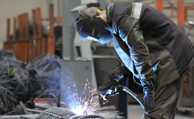 A machine operator working on a welding project while sparks and smoke emit.