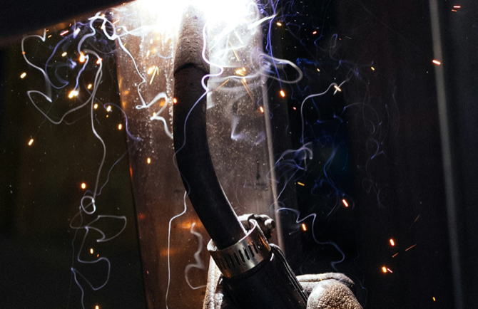 A welder's hand wearing a protective glove and welding on a project in a confined space.