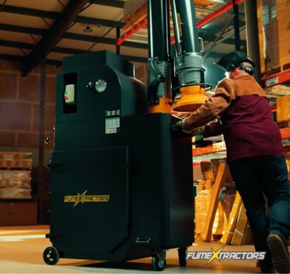 Machine operator pushing a portable fume extractor in an industrial space.