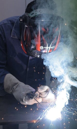 A masked welder working on a metalworking project while smoke and sparks arise.