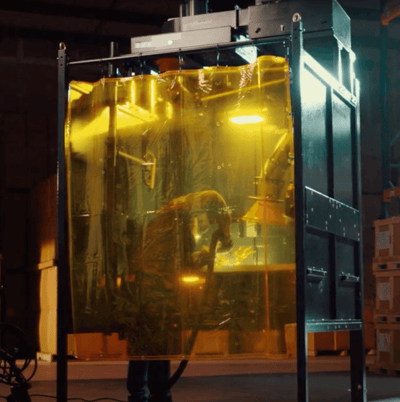 A welder working on a project inside of a Fume Xtractors welding booth while a fume extraction arm works to remove fumes.