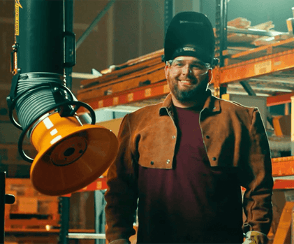 A welder in an industrial facility wearing PPE while standing next to a fume extraction arm that can be used for welding and grinding on explosive dust.