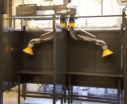 Welding booths with fume extraction arms and work benches installed in a high school workshop.